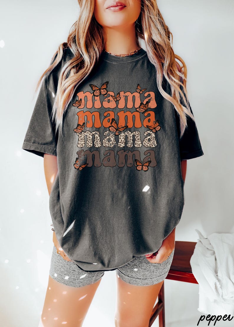 May include: A dark gray t-shirt with the text "mama mama mama mama" in a retro font with orange, brown, and white butterflies.