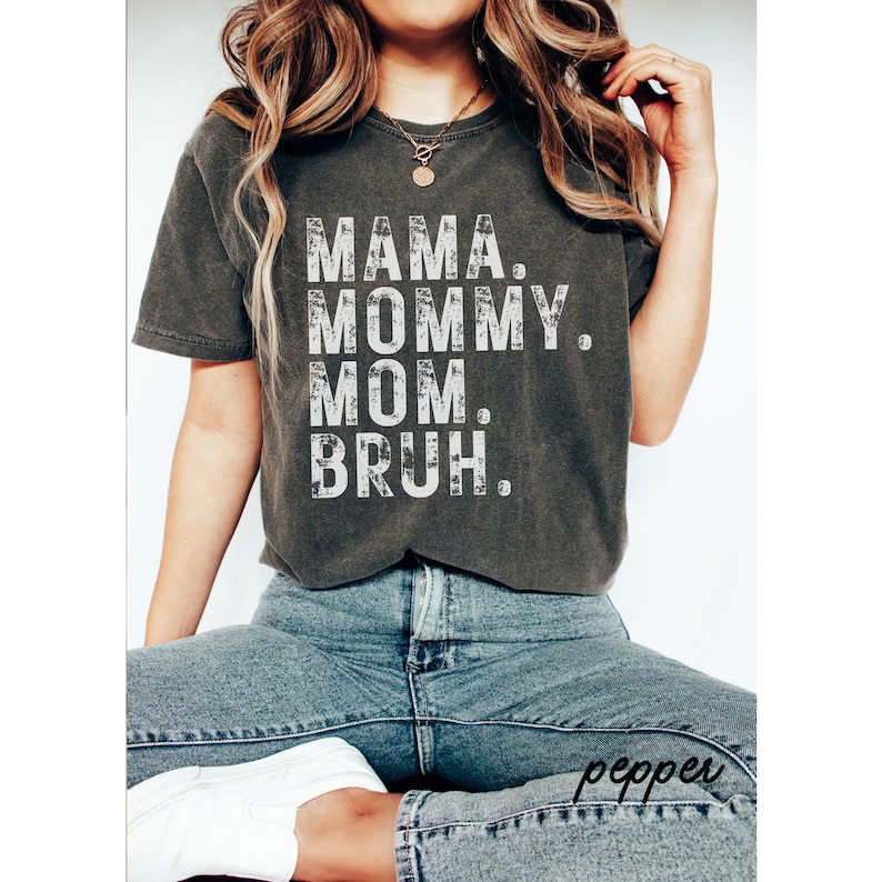 May include: A dark gray t-shirt with a white distressed graphic that reads "MAMA. MOMMY. MOM. BRUH."