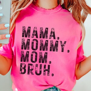 May include: Pink t-shirt with a black distressed graphic that reads "Mama. Mommy. Mom. Bruh."
