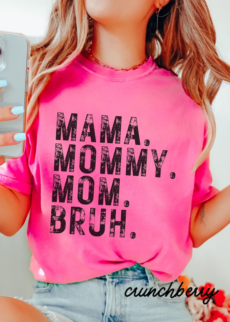 May include: Pink t-shirt with a black distressed graphic that reads "Mama. Mommy. Mom. Bruh."