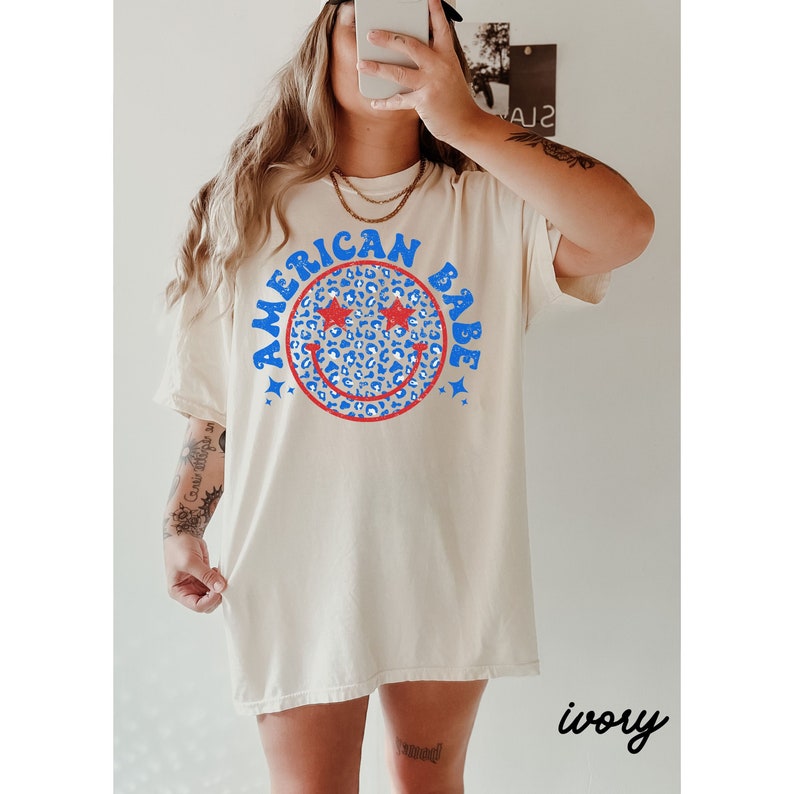 May include: A white oversized t-shirt with a blue and red smiley face graphic that says "American Babe". The smiley face has a leopard print pattern.