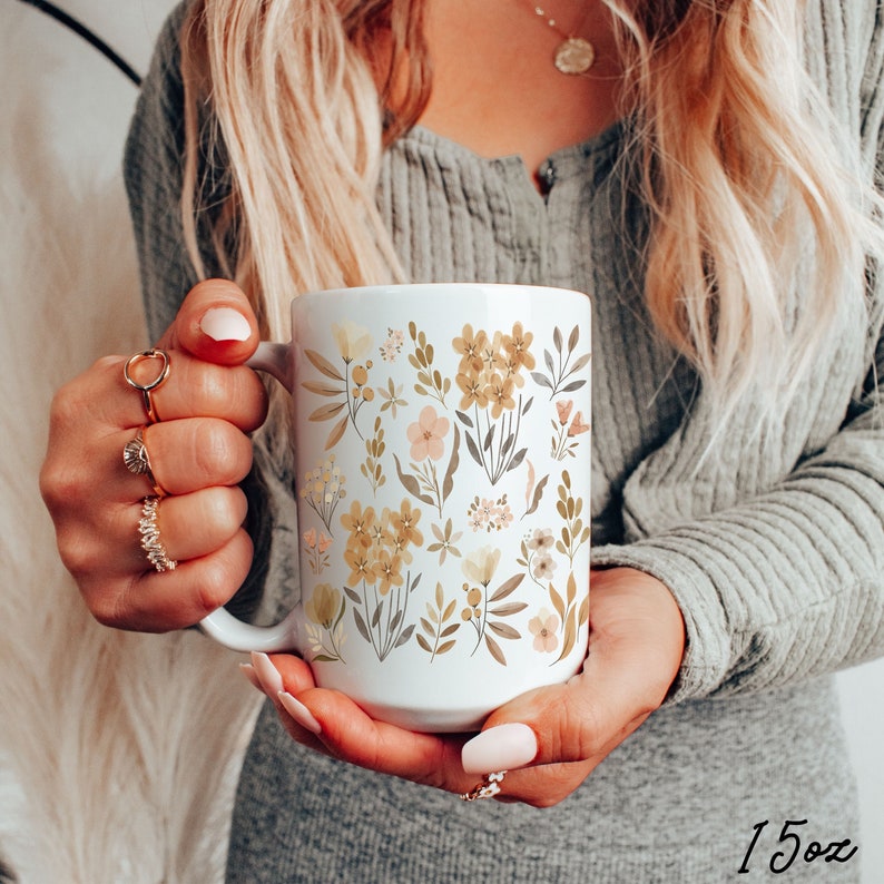 May include: White ceramic mug with a floral design featuring yellow, brown, and pink flowers and leaves. The mug is 15 oz.