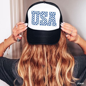 May include: A black and white trucker hat with a blue and white checkered "USA" graphic on the front.
