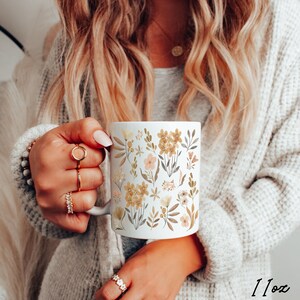 May include: White ceramic mug with a floral pattern in shades of brown, yellow, and pink. The mug features a variety of flowers and leaves, and the design is repeated all over the mug. The mug is 11 oz.