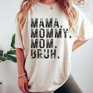 May include: A white t-shirt with black text that reads "MAMA. MOMMY. MOM. BRUH."
