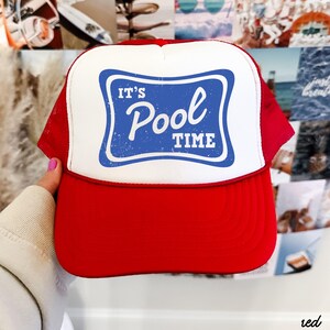 Może przedstawiać: Czerwono-biała czapka typu trucker z niebieskim prostokątem z napisem "It's Pool Time". Czapka ma czerwony daszek i siatkowy tył, idealna na basen lub plażę.