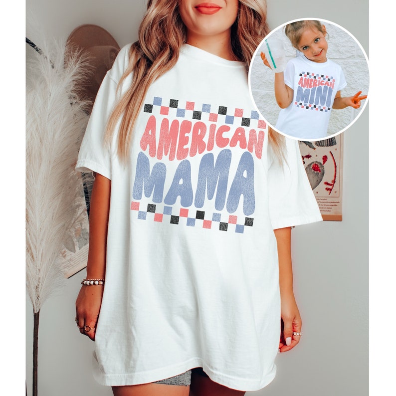 May include: White oversized t-shirt with the text "AMERICAN MAMA" in pink, blue, and black lettering with a checkered pattern.