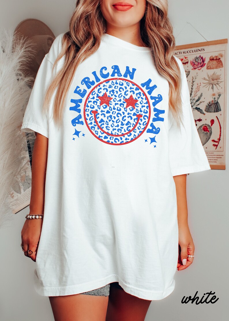May include: White oversized t-shirt with a blue and red smiley face graphic that says "American Mama". The smiley face has red stars for eyes and a leopard print pattern.