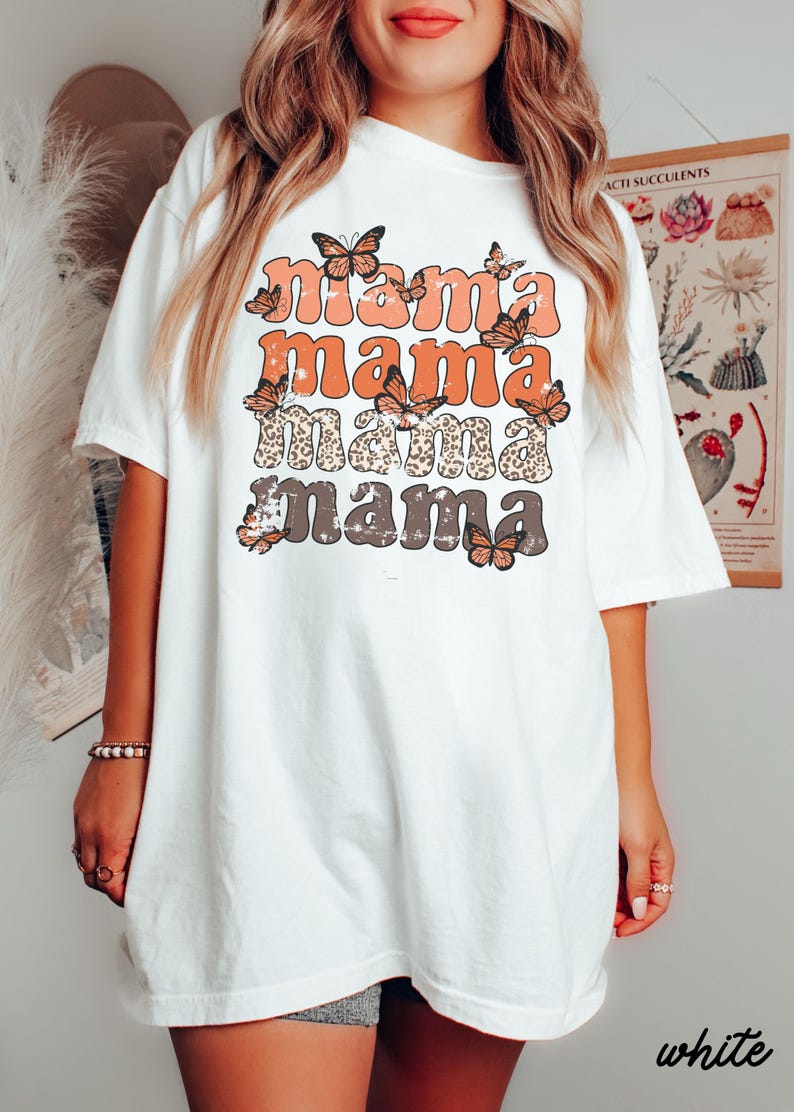 May include: White oversized t-shirt with a graphic design of the word "mama" repeated four times in different colors and styles. The word "mama" is surrounded by butterfly graphics.