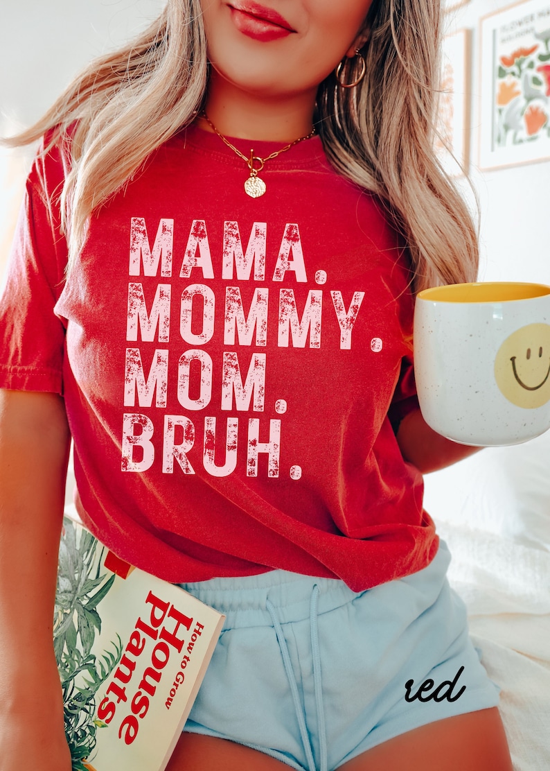 May include: Red t-shirt with the text "Mama. Mommy. Mom. Bruh." in pink lettering. The shirt is worn by a person wearing blue shorts with the word "red" written on the side.