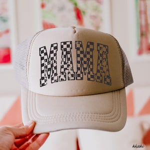 May include: A beige trucker hat with a black and white checkered "MAMA" graphic. The hat has a mesh back.
