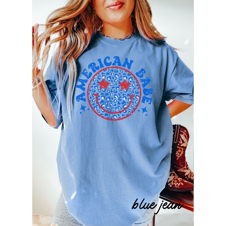 May include: A blue t-shirt with a red, white, and blue smiley face graphic with the text "American Babe" in a blue and white font.
