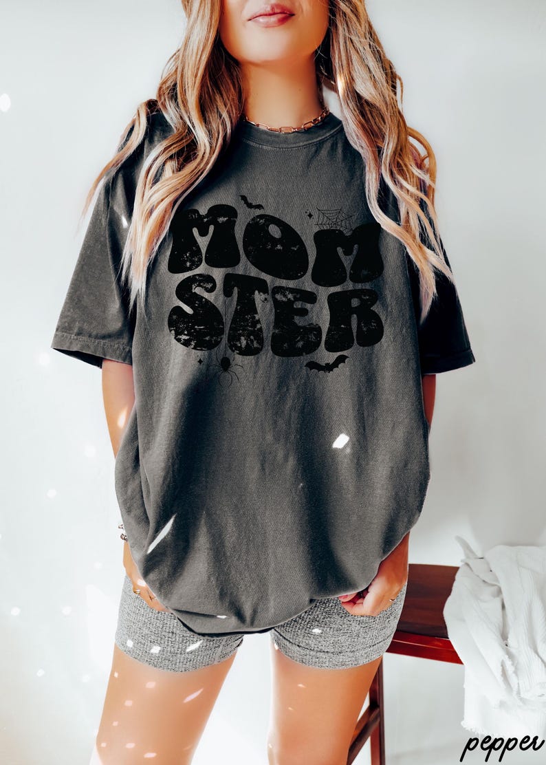 May include: A dark gray t-shirt with a black graphic that says "MOMSTER" in a retro font. The graphic also includes a spider web, bats, and stars.