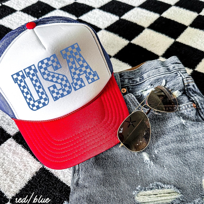 May include: A red and blue trucker hat with a white mesh back. The hat has a checkered "USA" design on the front.