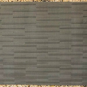 Puede incluir: Un mantel individual tejido gris con una textura sutil. El mantel individual es rectangular y tiene una superficie ligeramente rugosa.