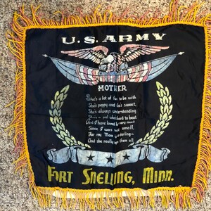 Puede incluir: Una almohada de satén negro con un borde de flecos amarillos. La almohada presenta una imagen impresa de un águila calva con las alas extendidas, un emblema del ejército de los Estados Unidos y un poema sobre una madre. El texto dice "U.S. ARMY", "MOTHER", "She's a lot of fun to be with", "She's peppy and she's sweet", "She's always understanding", "She's a pal who's hard to beat.", "And I have loved her very much", "Since I was very small", "For my Mom is a darling", "And she really tops them all", "FORT SNELLING, MINN."