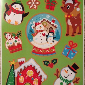 May include: A set of 10 Christmas window clings featuring a snowman, penguin, reindeer, house, and other festive designs. The clings are on a green background with the text "Window Decorations" and "Decorations Pour Fenetre".