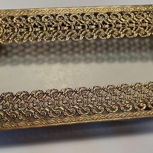 Pode incluir: Porta-guardanapos de metal dourado com um design decorativo de filigrana. O porta-guardanapos tem dois detalhes de pedra verde na parte superior e inferior.