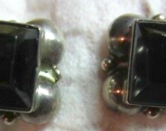 May include: A pair of silver earrings with black square-shaped gemstones set in a cluster of silver balls.
