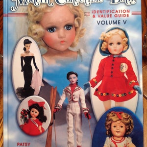 May include: A book titled "Modern Collectible Dolls: Identification & Value Guide, Volume V" featuring photos of various dolls. The cover features a blonde doll with blue eyes, a doll in a red and white ski outfit, a doll in a red dress, and a doll in a red and white dress.