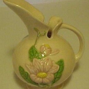 Peut inclure: Un pichet en céramique vintage avec un glacis jaune pâle et un motif floral. Le pichet présente des fleurs roses et vertes avec des centres jaunes.