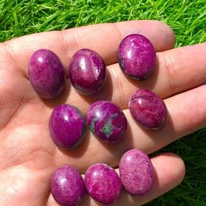 May include: Nine oval-shaped, cabochon cut, pink and green gemstones. The stones have a smooth, polished finish and are arranged in a hand.