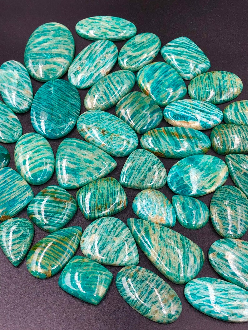 May include: A collection of green and white amazonite gemstone cabochons. The stones are smooth and polished, with a variety of shapes and sizes.