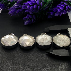 May include: Four silver pendants with a white, iridescent, and metallic finish. The pendants are round and have a geometric design. They are arranged in a row on a black surface.