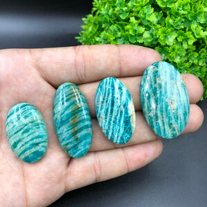 May include: Four oval-shaped green amazonite stones with white and brown stripes. The stones are smooth and polished.