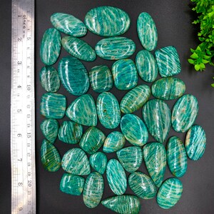 May include: A collection of 25 green and white amazonite cabochons. The cabochons are oval shaped and have a striated pattern.