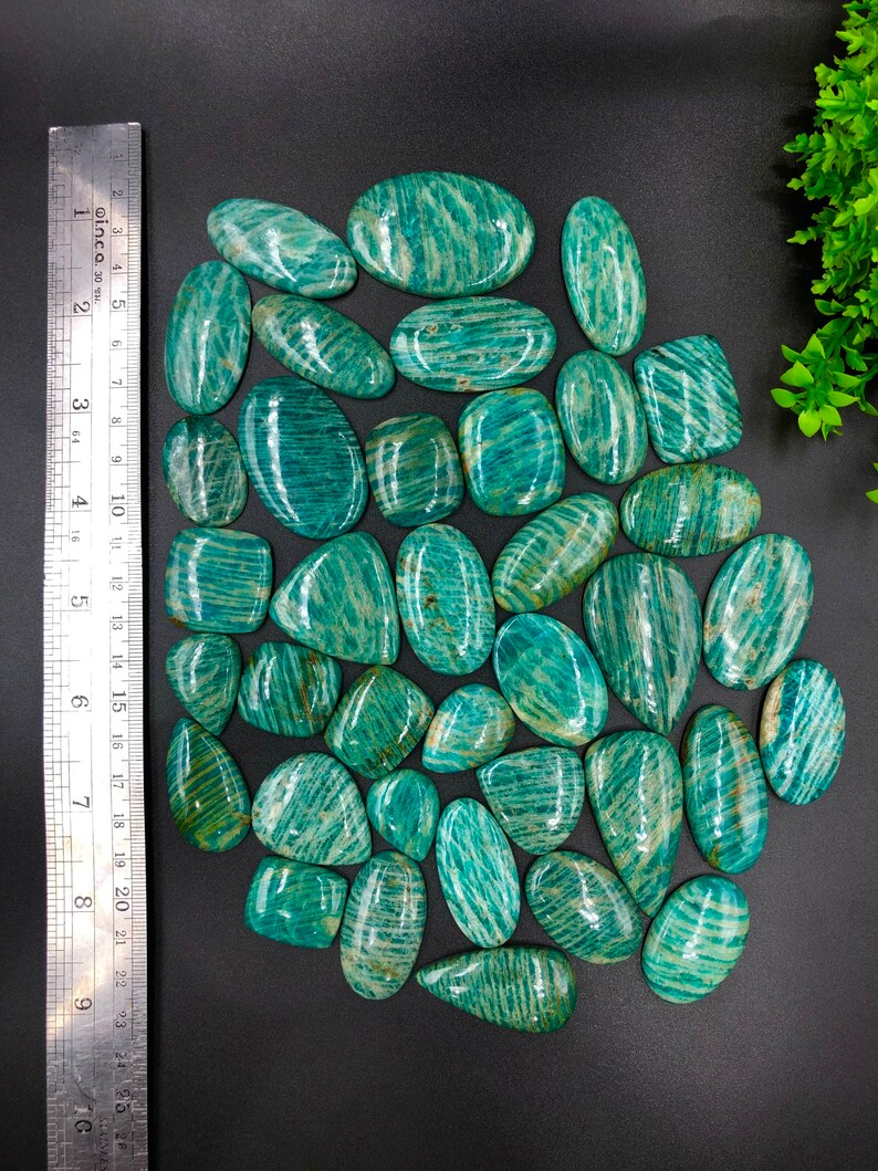 May include: A collection of 25 green and white amazonite cabochons. The cabochons are oval shaped and have a striated pattern.