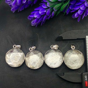 May include: Four silver pendants with a circular shape and a clear, white, textured surface. The pendants have a silver bail and are arranged in a row on a black surface.