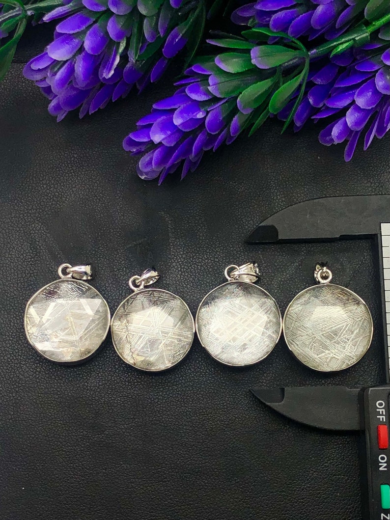 May include: Four silver pendants with a circular shape and a clear, white, textured surface. The pendants have a silver bail and are arranged in a row on a black surface.