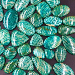 May include: A collection of green and white amazonite cabochons, each with a unique pattern of striations. The stones are smooth and polished, with a glossy finish.