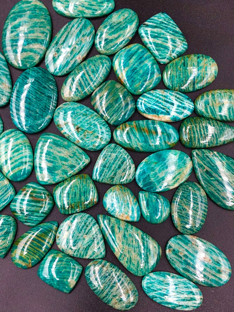 May include: A collection of green and white amazonite cabochons, each with a unique pattern of striations. The stones are smooth and polished, with a glossy finish.