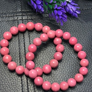Puede incluir: Dos pulseras de piedras preciosas rosas hechas de cuentas redondas. Las pulseras están hechas de una piedra rosa claro y están apiladas una encima de la otra.
