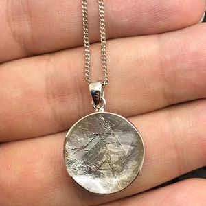 May include: A silver chain necklace with a round pendant featuring a slice of meteorite with a silver finish.
