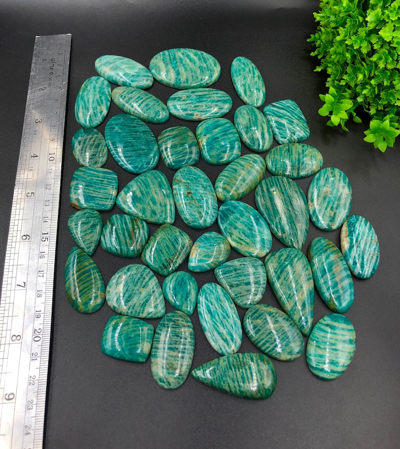 May include: A collection of 30 green amazonite cabochons, each with a unique striated pattern. The cabochons are various sizes and shapes, with a smooth, polished finish.