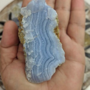 May include: A blue agate stone with white and light blue banding. The stone is rough and has a natural, unpolished finish.