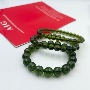 以下が含まれることがあります： 丸いビーズが付いた緑色の宝石のブレスレットが3つ。ブレスレットは重ねられています。