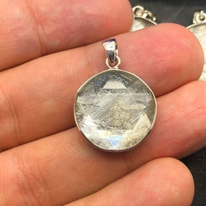 May include: A silver pendant featuring a round, clear, and translucent stone with a unique, intricate pattern of lines. The stone is set in a silver bezel.