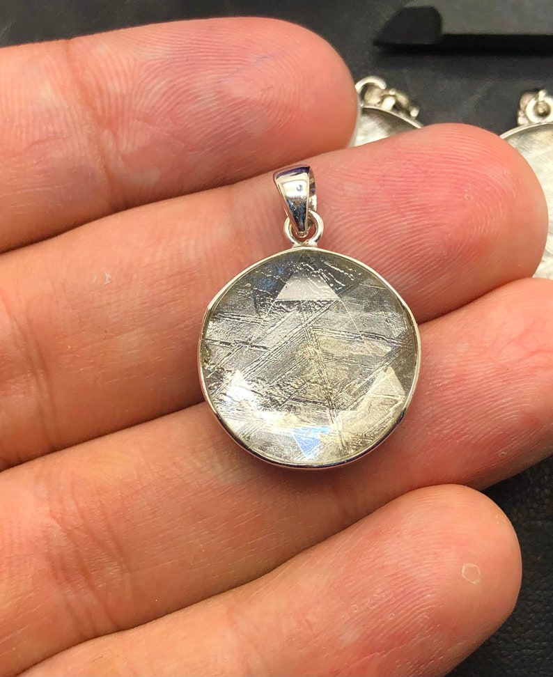 May include: A silver pendant featuring a round, clear, and translucent stone with a unique, intricate pattern of lines. The stone is set in a silver bezel.