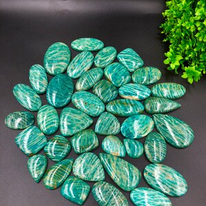 May include: A collection of 25 green amazonite gemstone cabochons with a striated pattern. The stones are various shapes and sizes, and have a polished finish.