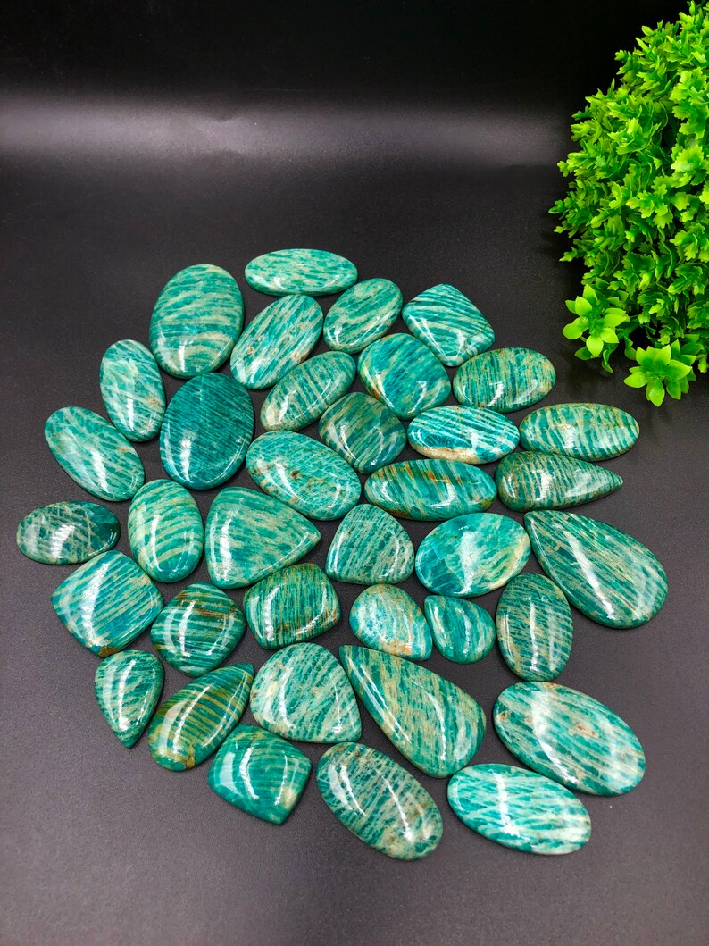 May include: A collection of 25 green amazonite gemstone cabochons with a striated pattern. The stones are various shapes and sizes, and have a polished finish.