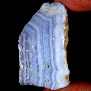 May include: A blue and white banded agate stone with a rough, natural edge. The stone has a light blue colour with white bands and a brown edge.