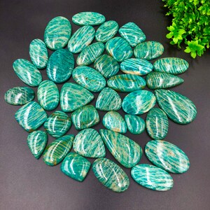 May include: A collection of 25 green and gold amazonite gemstone cabochons. The cabochons are all different shapes and sizes, but they all have a similar striated pattern. The cabochons are perfect for jewelry making or other crafts.