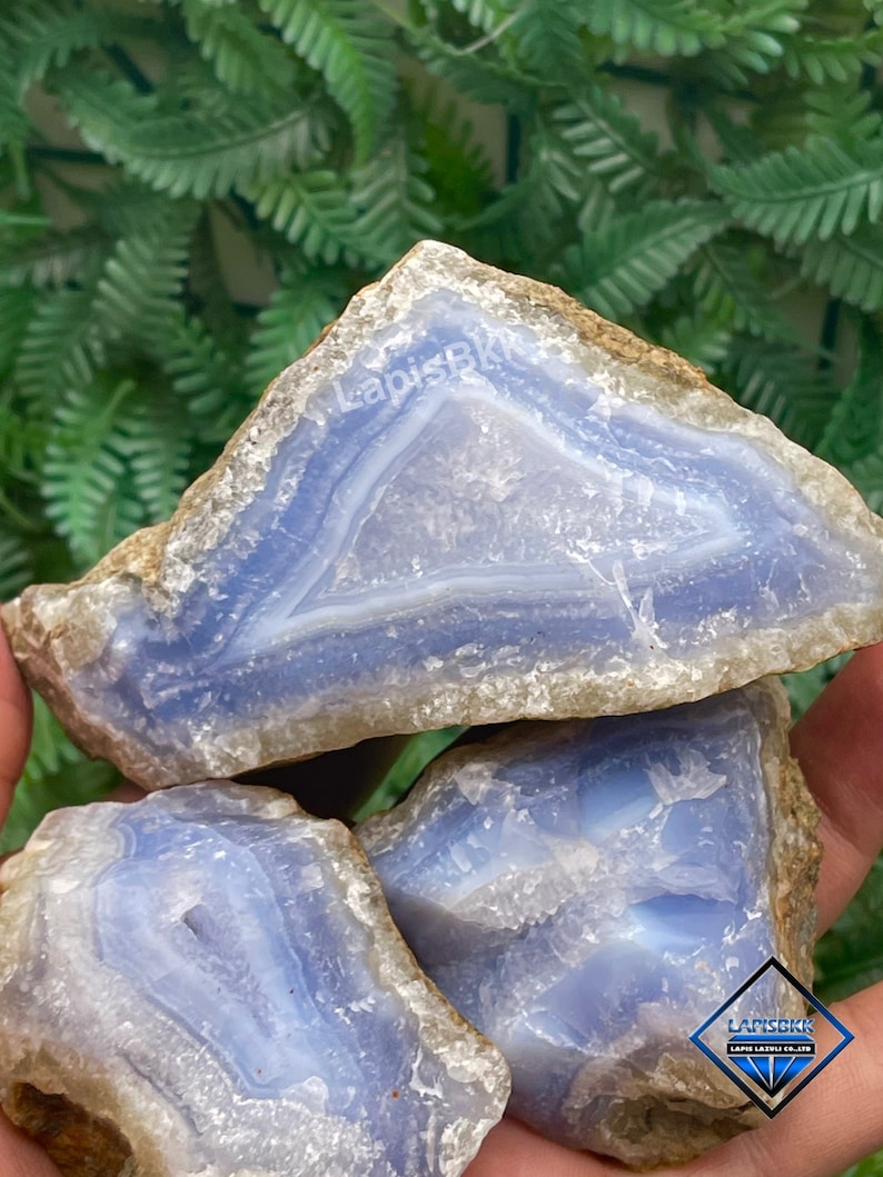 May include: Three blue agate stones with white and brown banding. The stones are stacked on top of each other. The top stone has the text "LapisBK" written on it.