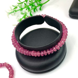 May include: A pink gemstone bracelet with a stretchy elastic band. The bracelet is displayed on a black velvet jewelry stand.