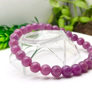 Op de afbeelding: Een armband van paarse edelstenen met ronde kralen. De armband ligt op een transparante standaard.