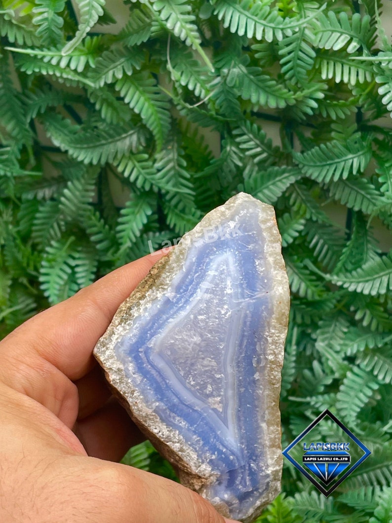 May include: A blue agate geode with a natural, rough exterior and a smooth, polished interior. The geode has a light blue colour with white bands and a white centre. The geode is approximately 10 cm tall and 7.5 cm wide.